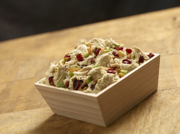 Shredded chicken salad with dried cranberries, golden raisins and green onions in a square wood catering box