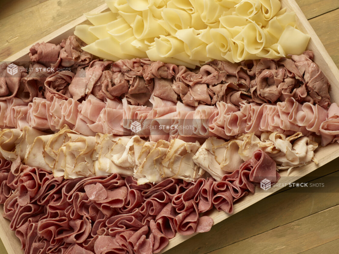 Deli meat and cheese tray on a wood catering tray on a wooden background