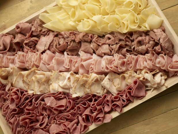 Deli meat and cheese tray on a wood catering tray on a wooden background
