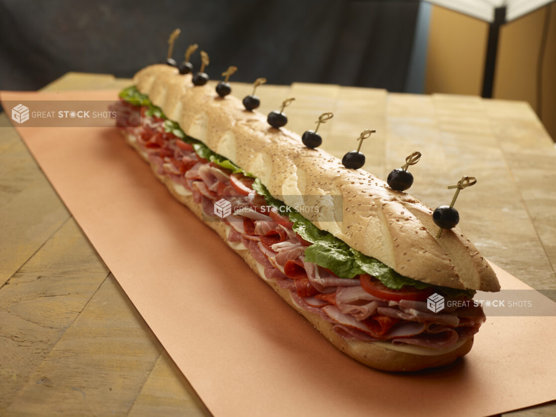 Giant assorted submarine sandwich with various meats, cheese, lettuce and tomatoes with bamboo skewered black olives