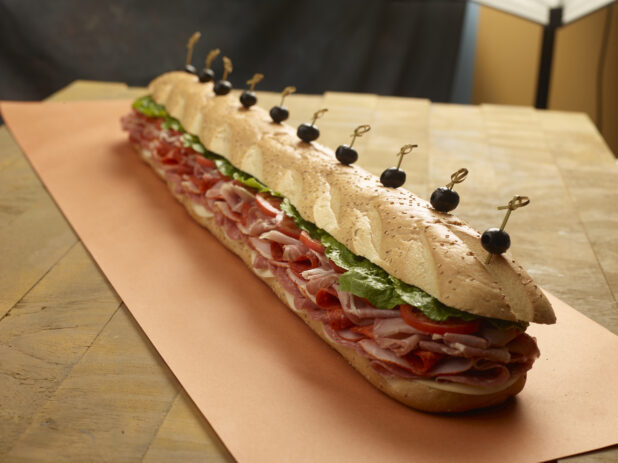 Giant assorted submarine sandwich with various meats, cheese, lettuce and tomatoes with bamboo skewered black olives