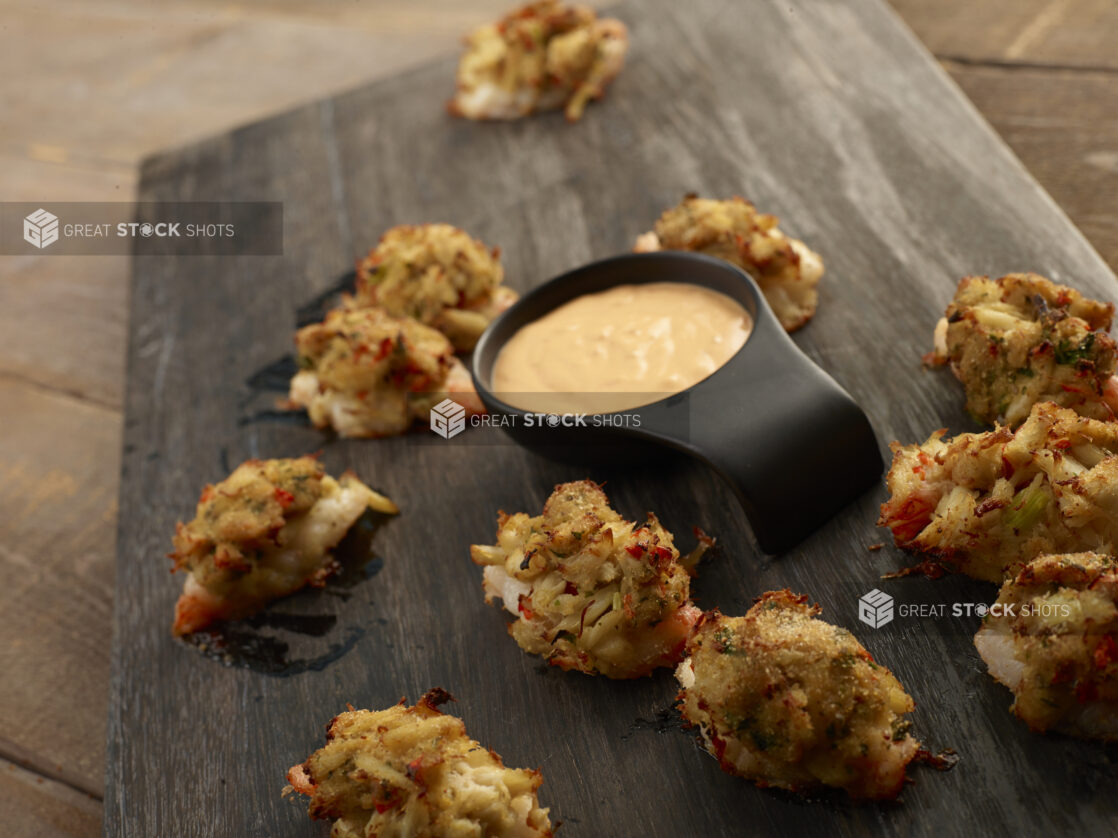 Clusters of lobster fritters with a dipping sauce on a wooden board