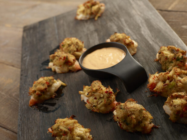 Clusters of lobster fritters with a dipping sauce on a wooden board