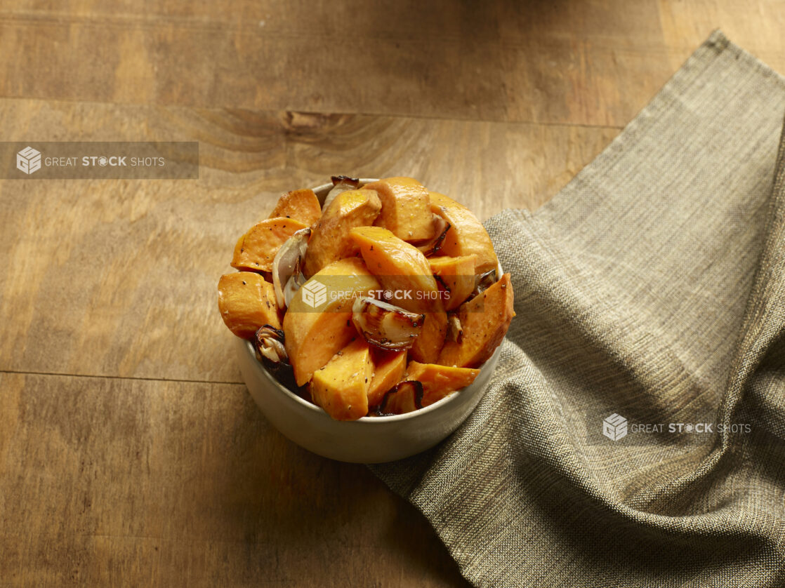 Overhead of small bowl of roasted sweet potato with garlic and onions on a wood table