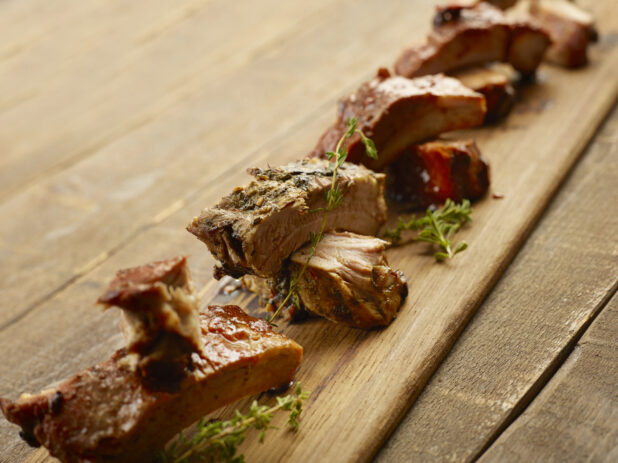 Wooden board of different flavored ribs on a wood table with fresh herbs