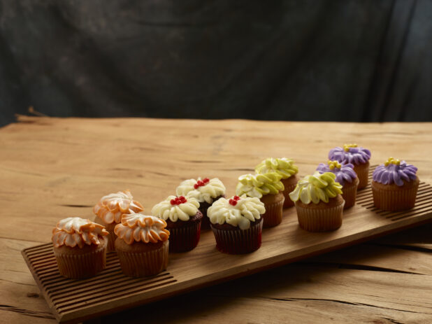 Cupcakes with an elegant floral design, multiple colours, on a wooden board, wooden background