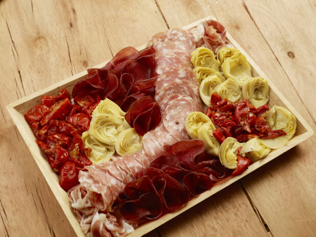 Antipasto wood tray of cured meats, artichoke and sun-dried tomatoes on a wood table