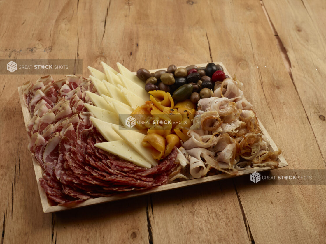 Charcuterie wood tray of cured meats, cheese, roasted pepper and olives on a wood table