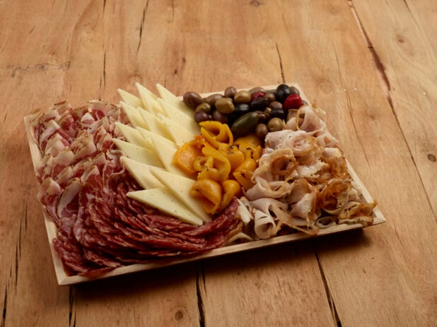 Charcuterie wood tray of cured meats, cheese, roasted pepper and olives on a wood table