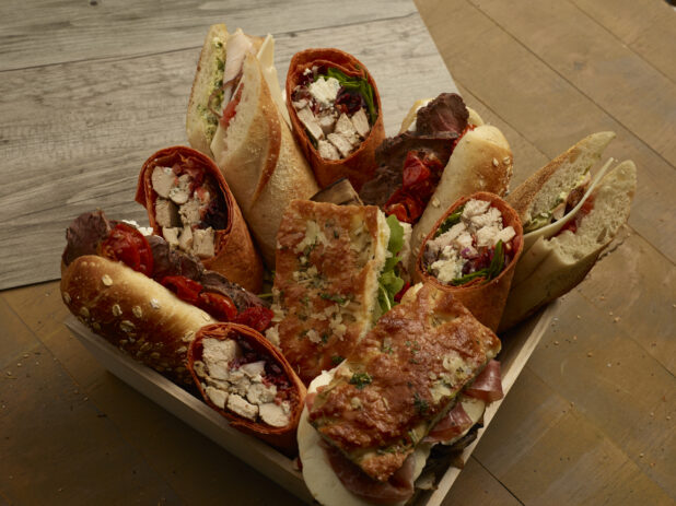 Assorted artisanal sandwiches and wraps in a wood catering box on a wooden background