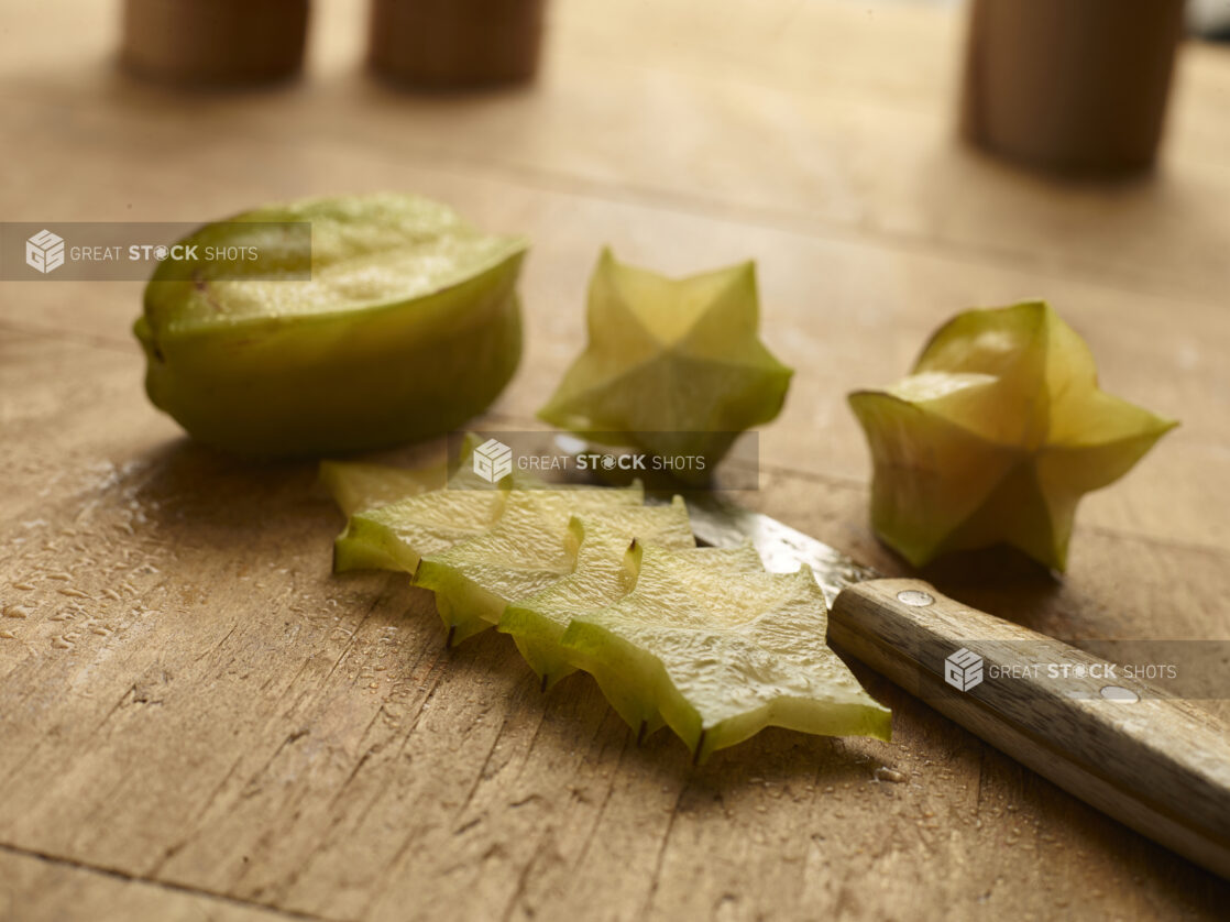 whole and sliced star fruit on a wood table with a knife