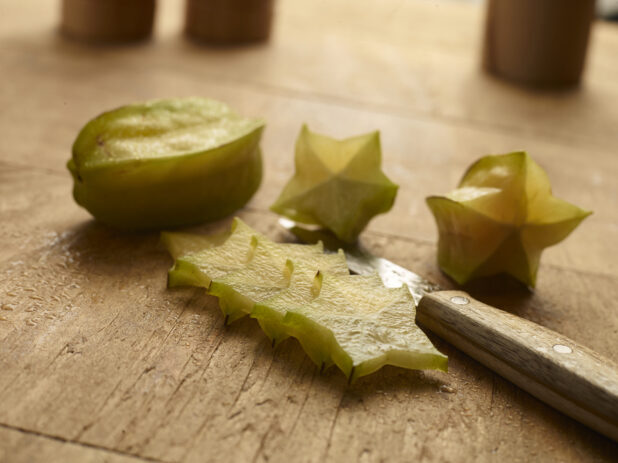whole and sliced star fruit on a wood table with a knife