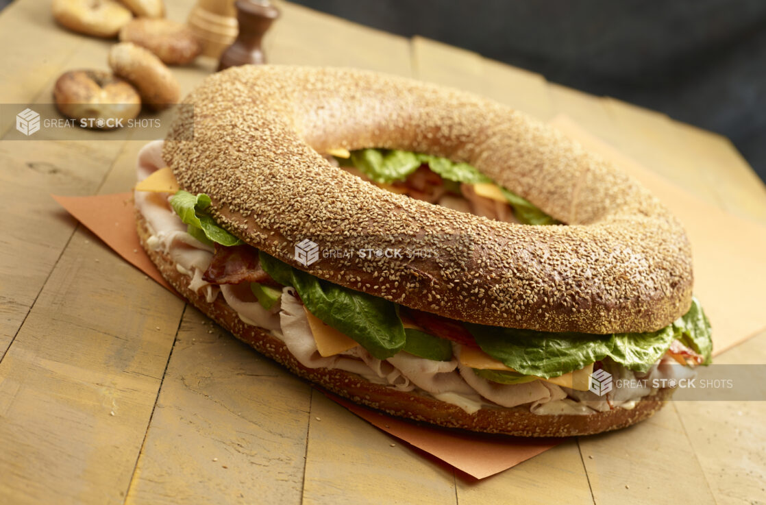 Giant sesame turkey club bagel with cheese with whole uncut bagels in the background