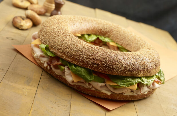 Giant sesame turkey club bagel with cheese with whole uncut bagels in the background