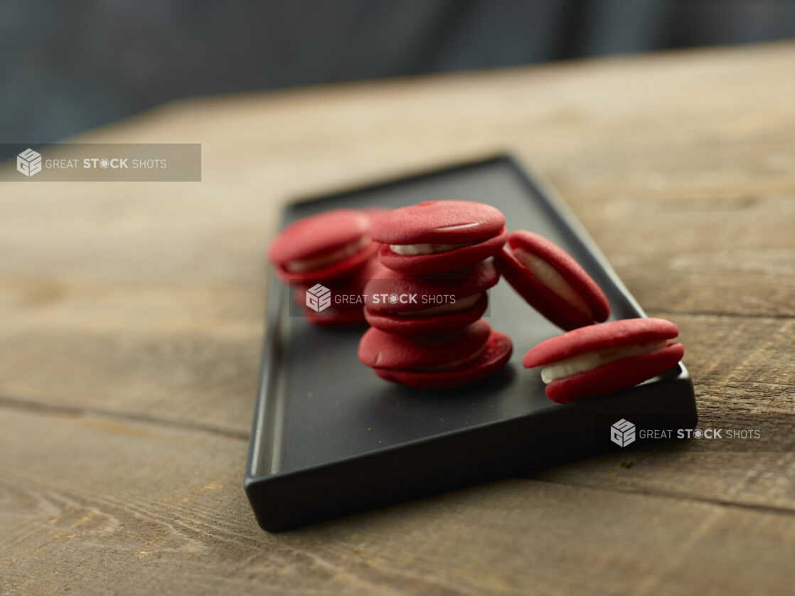 Group of red macrons on a black platter on a wood table