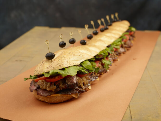 Giant submarine sandwich with roast beef, caramelized onions, tomatoes, lettuce and cheese