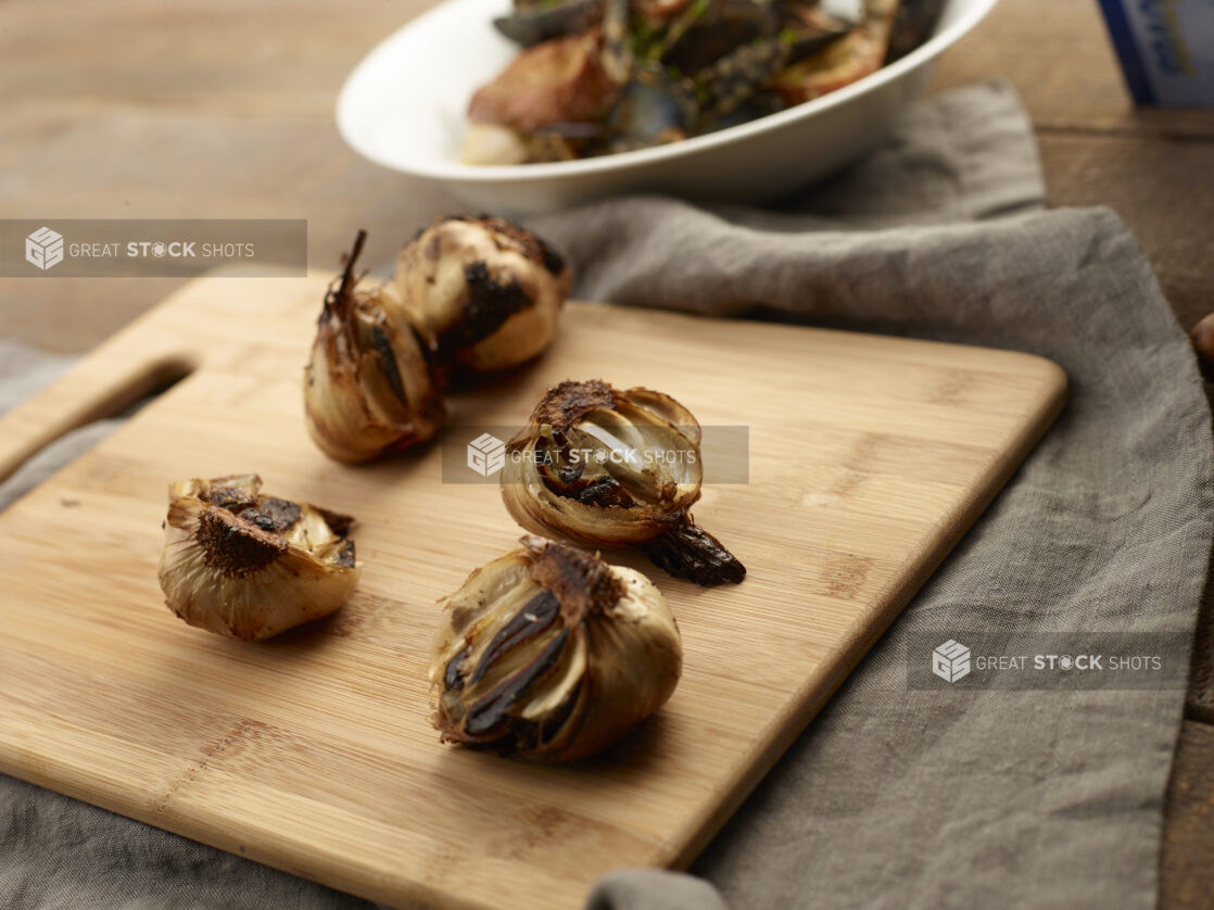 Charred garlic bulbs cut in half on a wooden cutting board