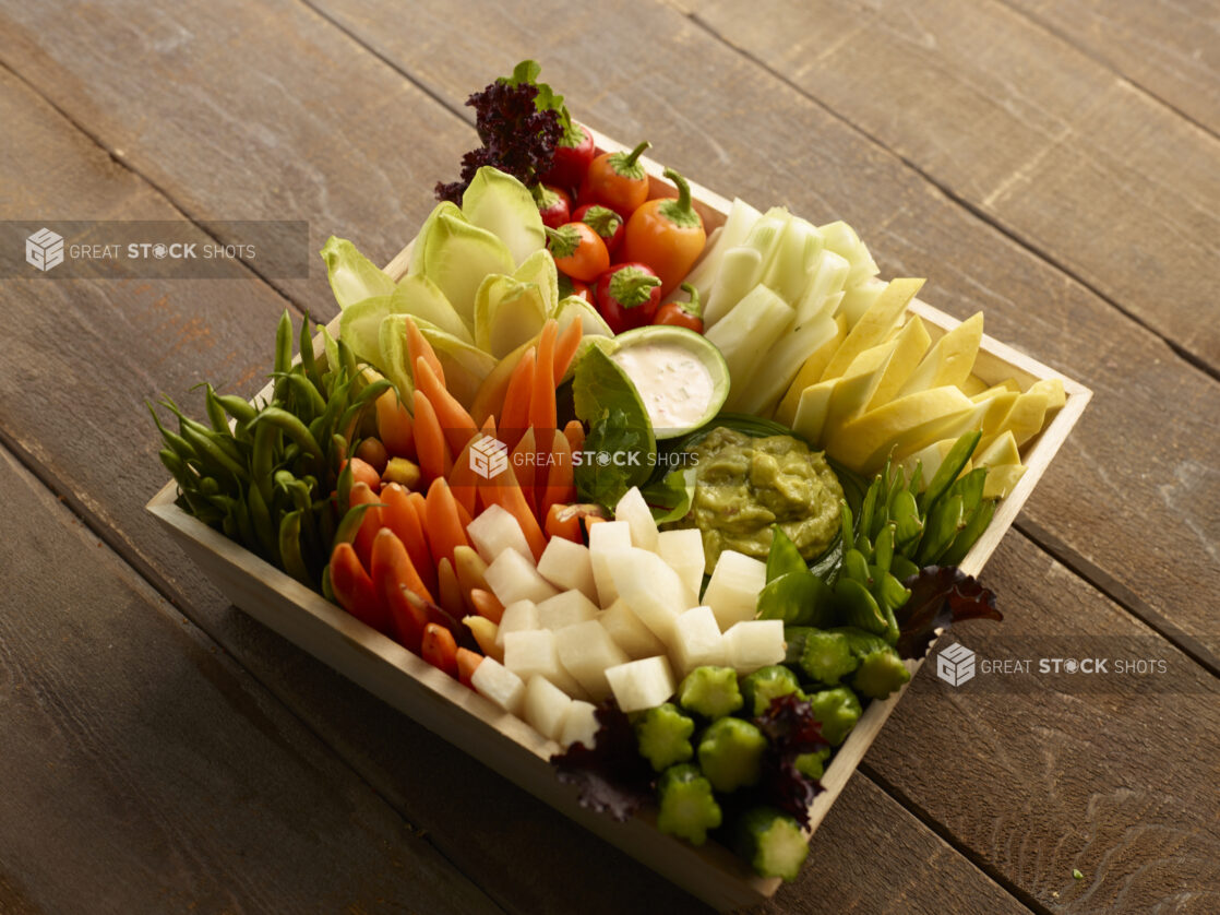 Overhead of wood tray vegetable platter with dips on a wood table