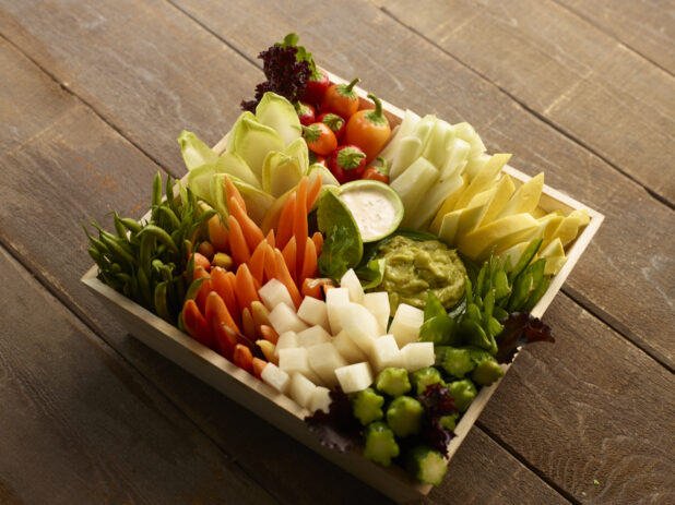 Overhead of wood tray vegetable platter with dips on a wood table