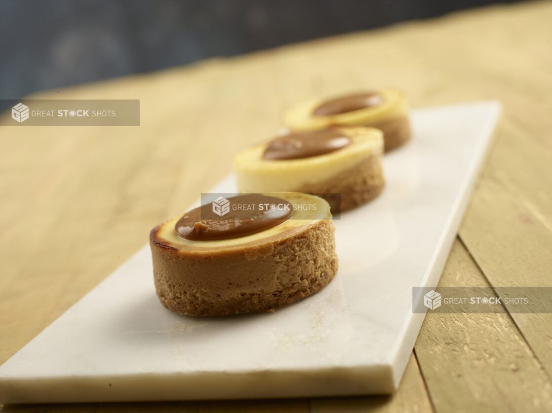 Mini caramel cheesecakes on a white marble slab on a wooden background