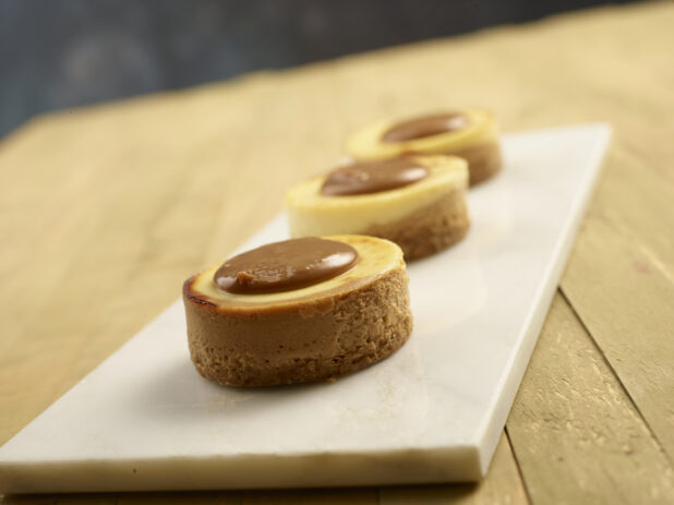 Mini caramel cheesecakes on a white marble slab on a wooden background