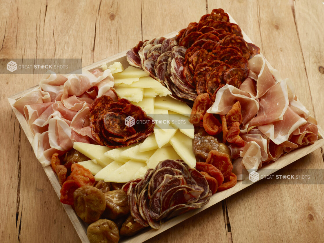 Charcuterie wood tray of cured meats, cheese and dried fruits on a wood table