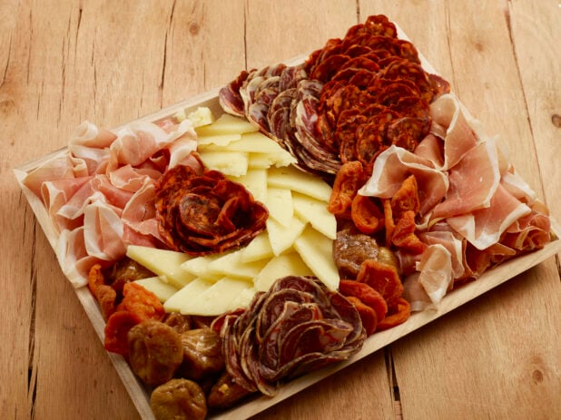 Charcuterie wood tray of cured meats, cheese and dried fruits on a wood table