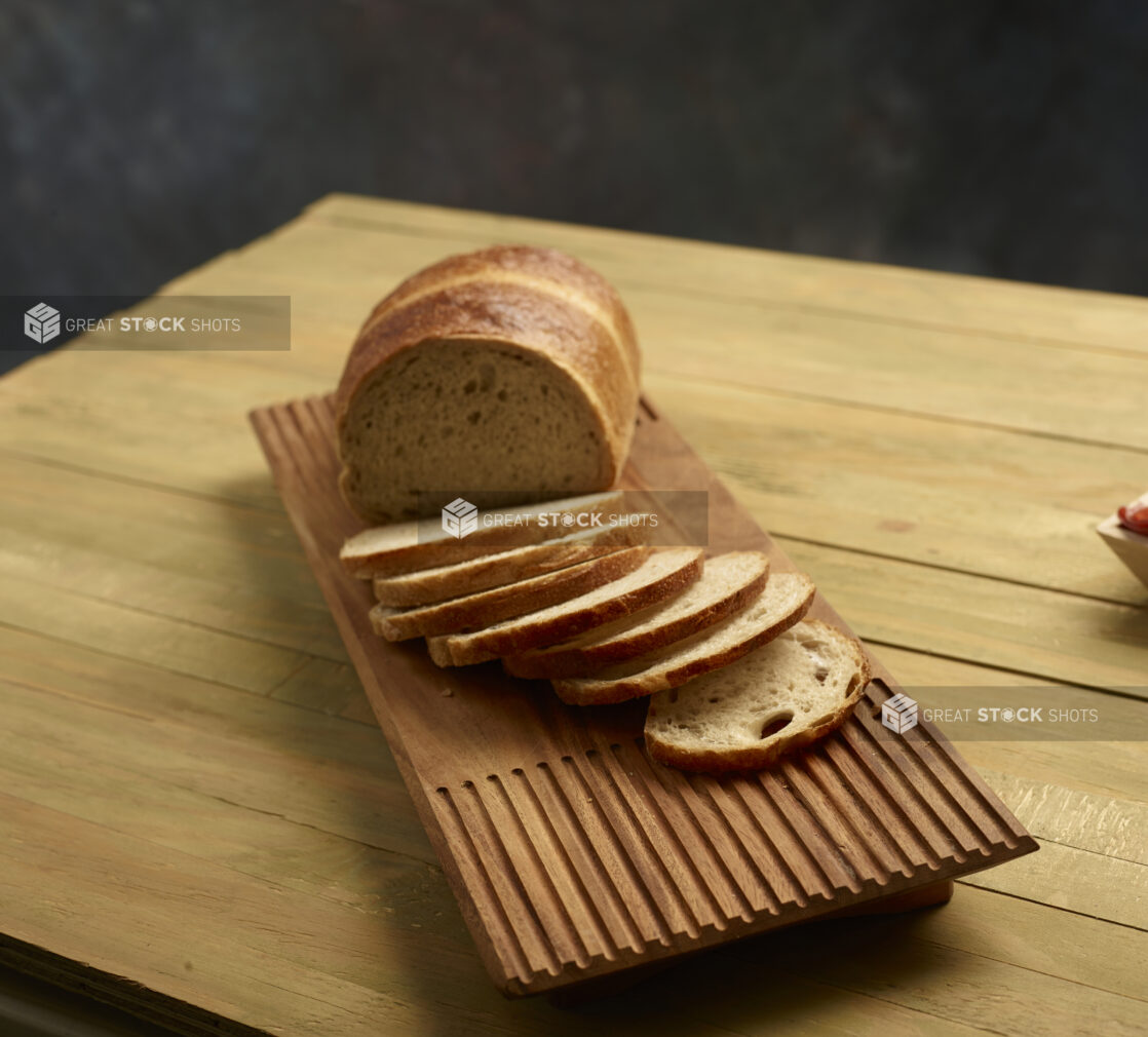 Light rye bread, half sliced, half unsliced, on wooden board on a wooden background