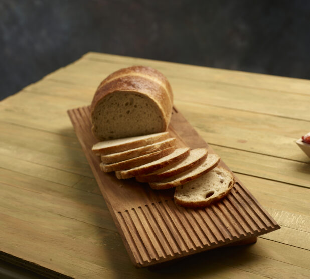 Light rye bread, half sliced, half unsliced, on wooden board on a wooden background