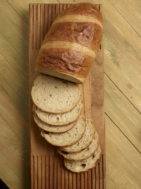 Loaf of light rye bread, half sliced, half unsliced, on wooden board on a wooden background, overhead view