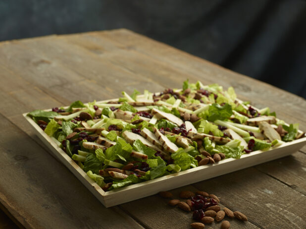 Wood catering tray of grilled chicken salad with green apple, almonds and dried cranberries on a wood table