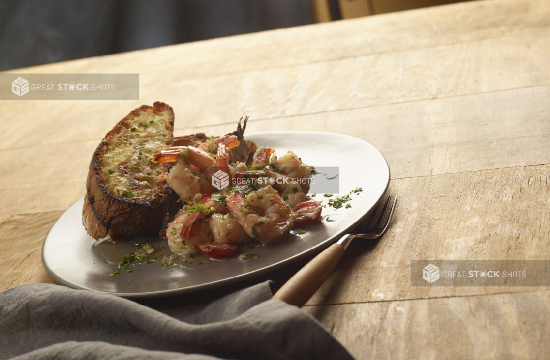 Garlic butter herb shrimp with toasted garlic bread on a plate on a wood table