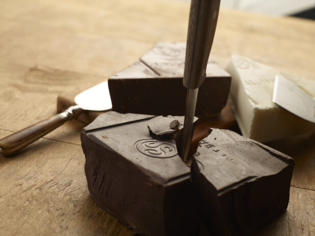 Chuncks of dark, white and milk chocolate being broken up by a knife on a wood table