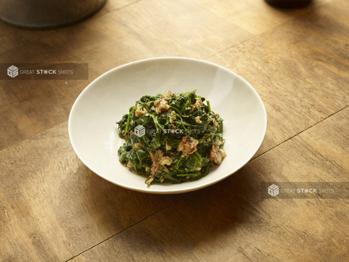 Rapini with XX in a shallow white bowl on a wood tabletop