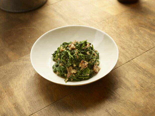 Rapini with XX in a shallow white bowl on a wood tabletop