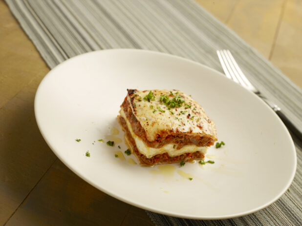 Square piece of meat lasagna on a large white plate on a wood table