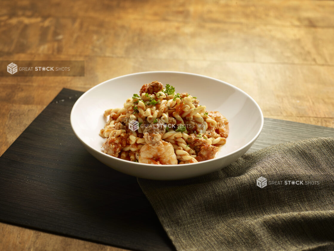 Bowl of cajun pasta with shrimp and sausage in a tomato sauce on a wood board