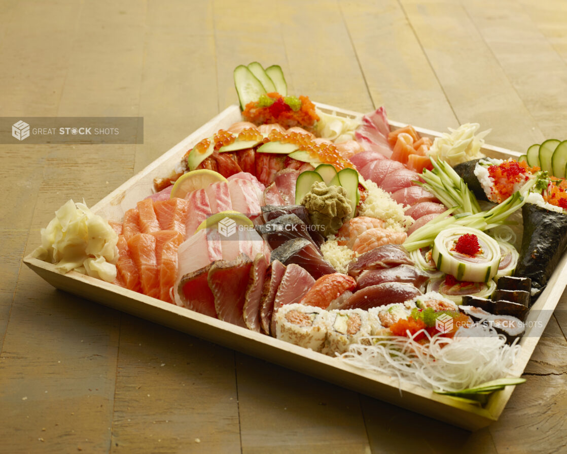 Large wood catering tray filled with sushi, sashimi, maki rolls, fresh ginger and wasabi on a wood table