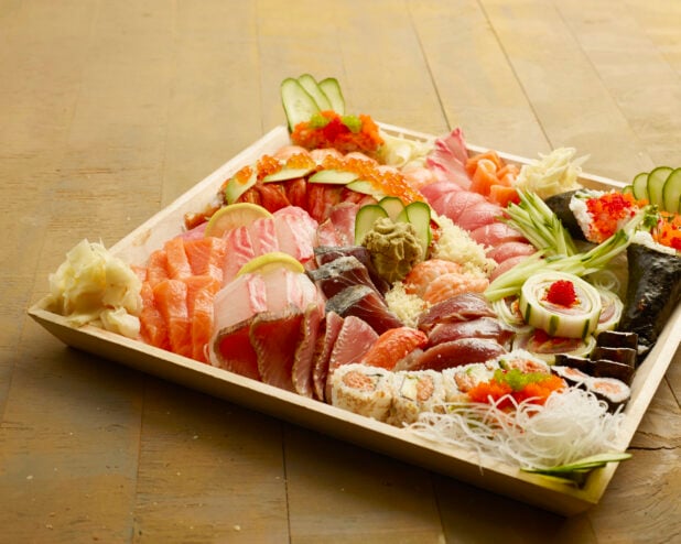 Large wood catering tray filled with sushi, sashimi, maki rolls, fresh ginger and wasabi on a wood table