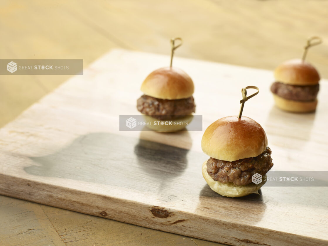 Three plain sliders on a wooden board with bamboo toothpicks on a wood table