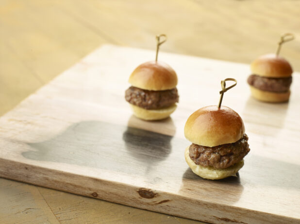 Three plain sliders on a wooden board with bamboo toothpicks on a wood table