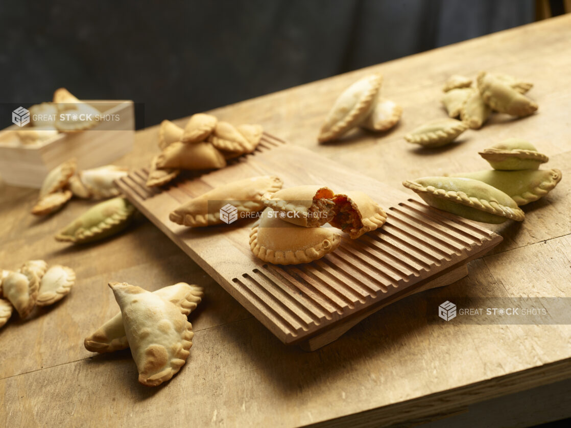 Collection of different flavored empanadas with one cut in half on a wooden board on a wood table