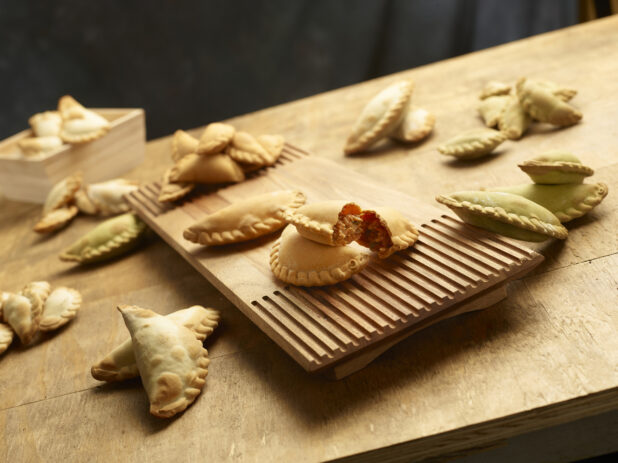 Collection of different flavored empanadas with one cut in half on a wooden board on a wood table
