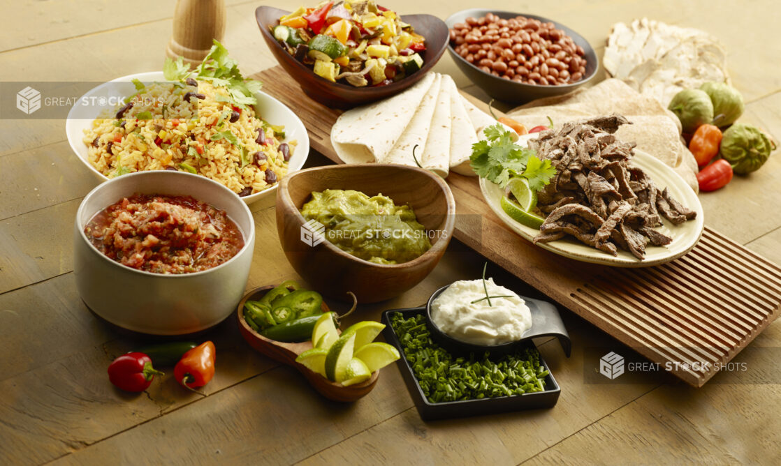Bowls of Mexican food and toppings to make steak fajitas on a wood table