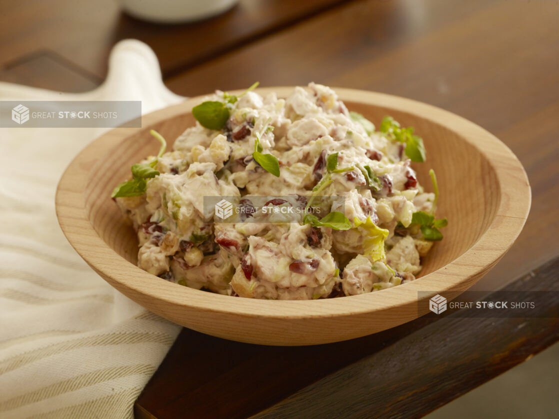 Wooden bowl of creamy cranberry chicken salad with golden raisins and celery on a wood table