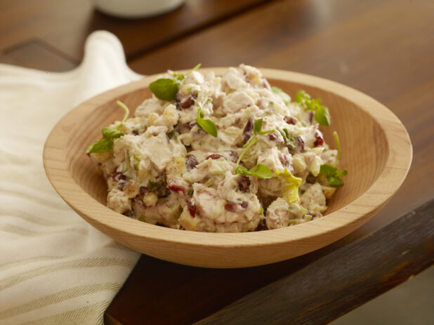 Wooden bowl of creamy cranberry chicken salad with golden raisins and celery on a wood table