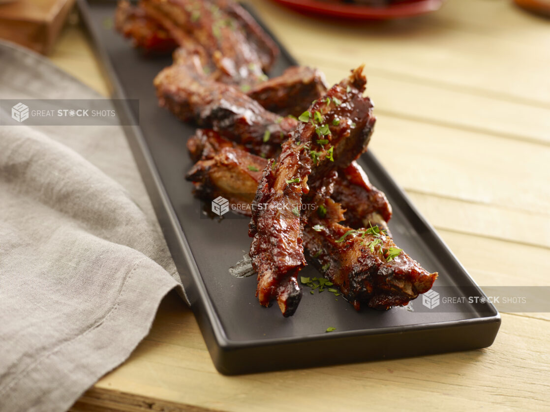 Sauced and seasoned pork ribs on a black platter on a wood table