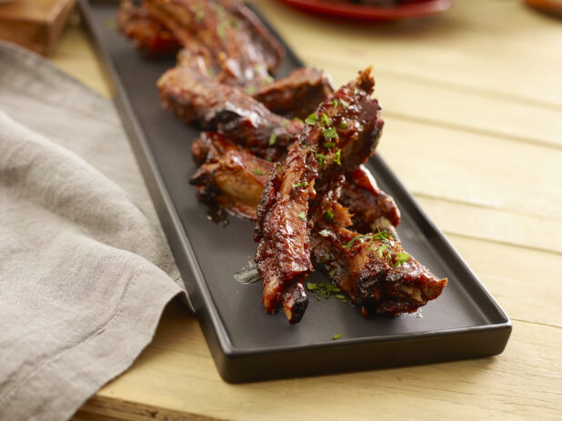 Sauced and seasoned pork ribs on a black platter on a wood table