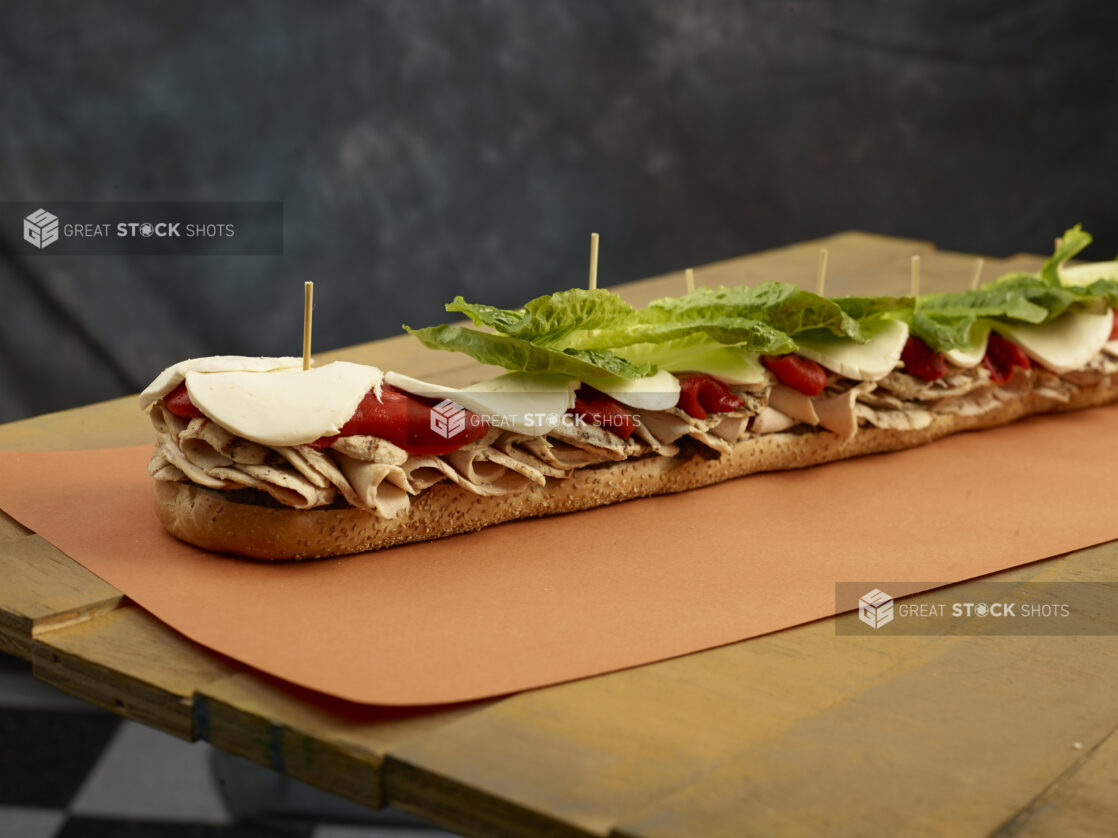 Inside look at a giant submarine sandwich with roasted chicken, roasted red peppers, lettuce and cheese on a sesame seed baguette