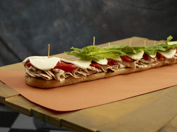 Inside look at a giant submarine sandwich with roasted chicken, roasted red peppers, lettuce and cheese on a sesame seed baguette